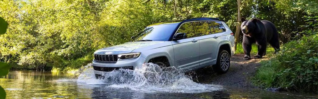 2026 Jeep Grand Cherokee crossing water with a bear nearby 