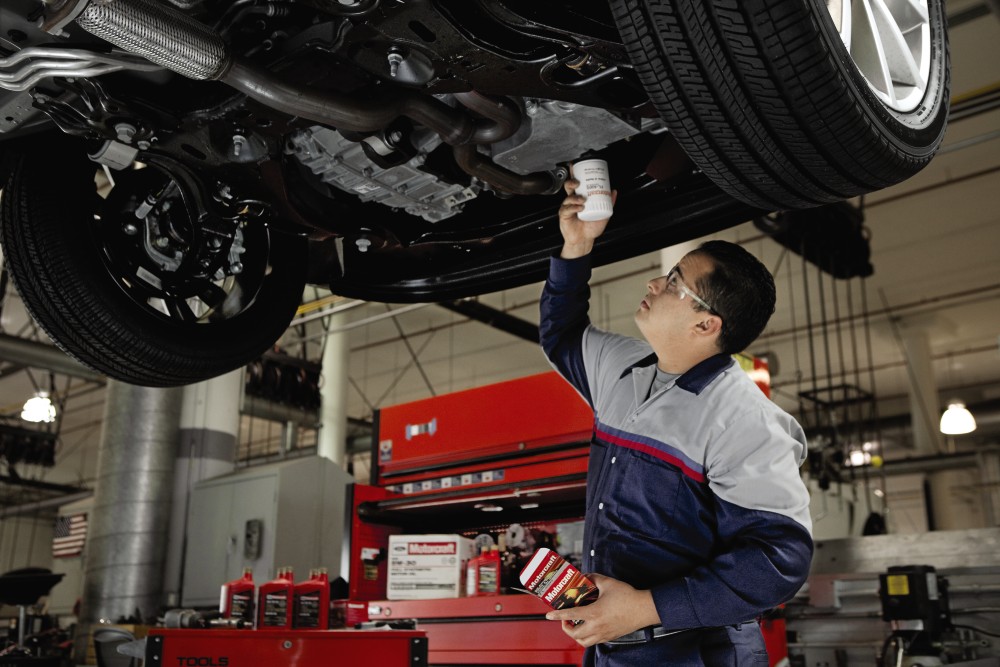 Mechanic performing an oil change under a RAM truck in a workshop