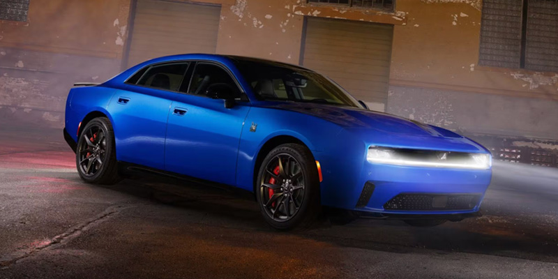 A blue Dodge Charger parked in an industrial setting with dramatic lighting, showcasing its sleek design and performance features.
