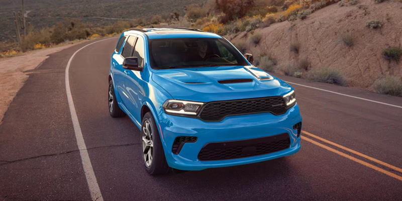 Blue Dodge Durango SUV driving on a winding road through a scenic landscape