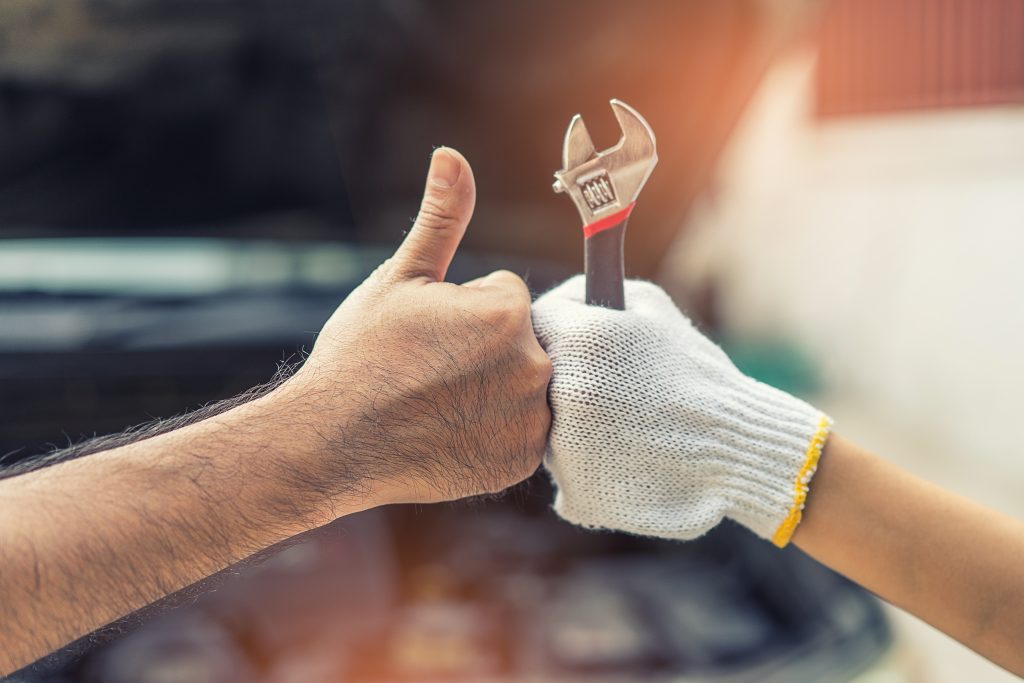 Mechanic holding a wrench and giving a thumbs-up during vehicle service