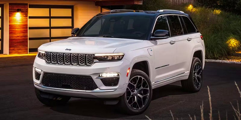 White Jeep Grand Cherokee SUV parked outside a modern home at dusk.